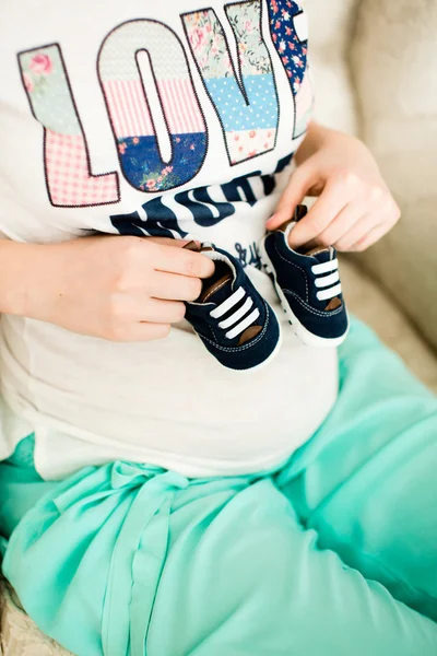 Pregnant woman holding small baby shoes