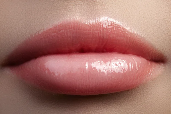 Close-up beautiful female lips with bright lipgloss makeup. Perfect clean skin, light fresh lip make-up. Beautiful spa macro shot with tender pink lip gloss. Spa and cosmetics
