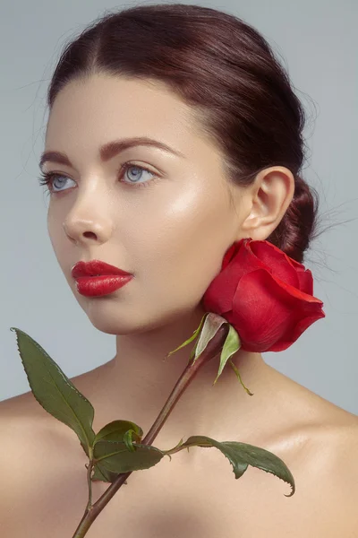 Close-up beautiful young woman with bright lipgloss makeup. Perfect clean skin, sexy red lip make-up. Beautiful valentine visage with red rose flower. Romantic and sexy look for Valentines day