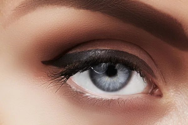 Close-up macro of beautiful female eye with perfect shape eyebrows. Clean skin, fashion naturel make-up. Good vision. Classic fashion eye liner makeup. Black eyeliner and brown eyeshadows