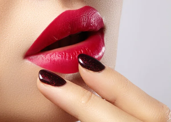 Close-up of woman\'s lips with fashion red make-up and manicure. Beautiful female full lips with perfect makeup. Classic visage. Part of female face. Macro shot of beautiful make up on full lips.