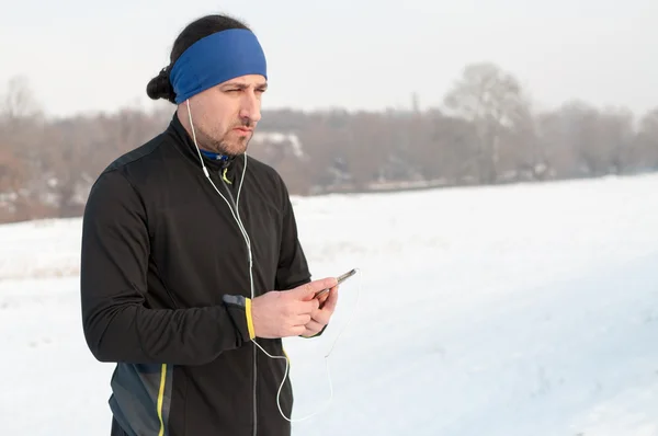 Male runner listen music from smartphone on winter day
