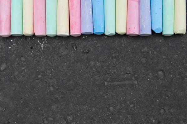 Colorful pastel sidewalk chalk on dark asphalt background.