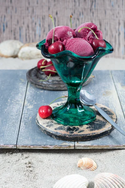 Fresh cherry ice-cream scoops in glass cone on the beach, summer