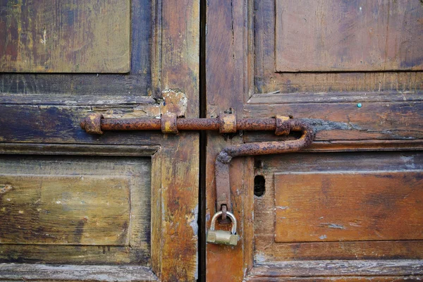 Detail of a metal door latch with padlock on an ancient wooden door