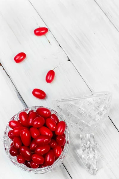 Cornel berries crystal glass on white wooden background, selecti