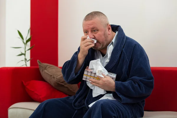 Man having a cold holding tissue with box full of tissues
