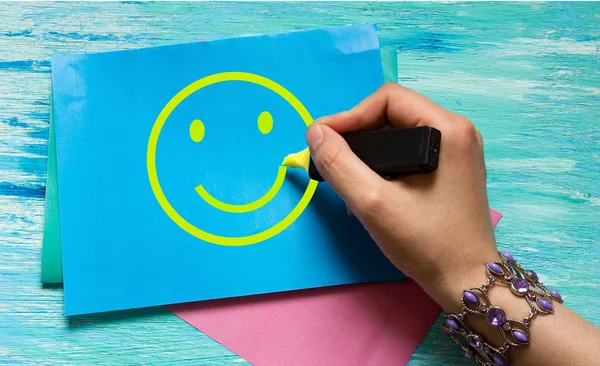 Smiley women's hand drawing on a blue sheet with a yellow marker. the concept of happiness, good mood, can be used for ads, postcards