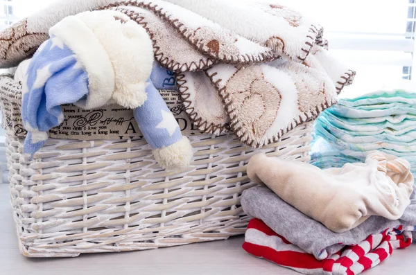 Grey basket with childrens toys, diapers, accessories on table on grey wooden background. Mother care. childrens room, the pile of blue clothes for newborn boy