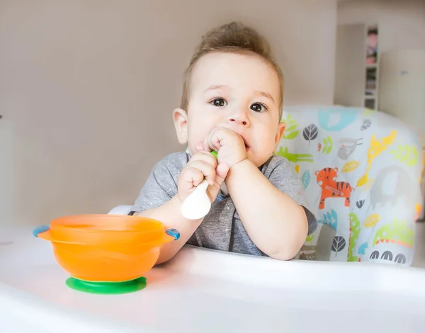 Small happy child sitting in a chair and eats from whose face is marred in baby food, the concept of family, child health, feed the baby, eat at home