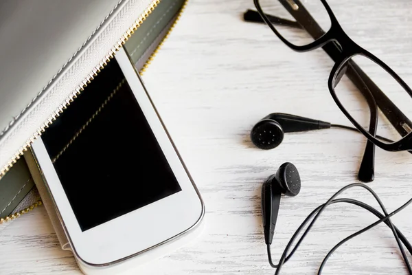 Top view on things women bag. image smartphone with blank screen, headphones, room for text. overhead of office Desk, glasses, clutch, copy space