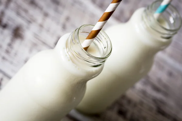 Two bottles of milk with striped straws standing on old table.