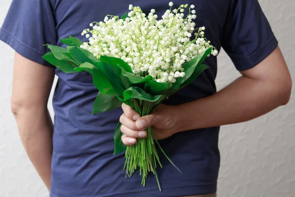 A man holding a bouquet of lilies of the valley for women. A man