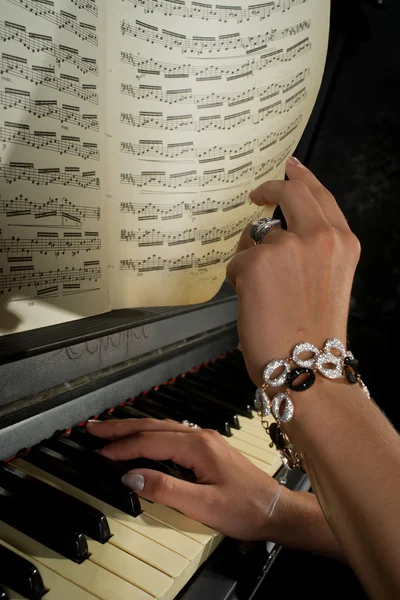 The girl plays the piano, hands, music notes, keys closeup