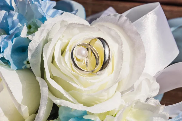 Silver wedding rings are on petals of artificial rose