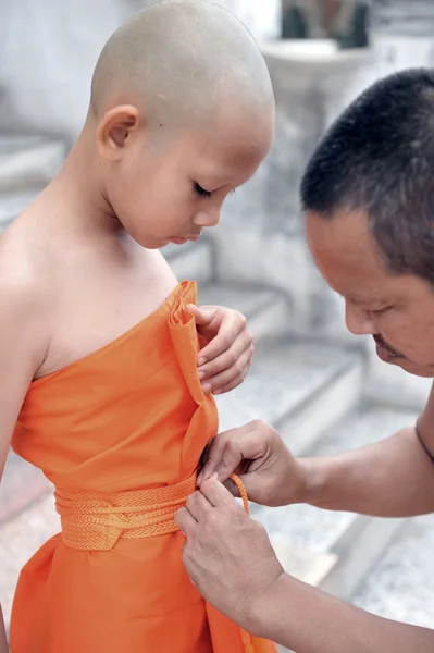Old Buddhist monk helps young novice monk wearing yellow robe during the ordinate ceremony