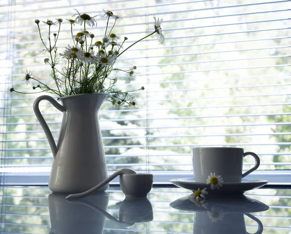 Bouquet of daisies and cup of tea on glass table background window. still life in white