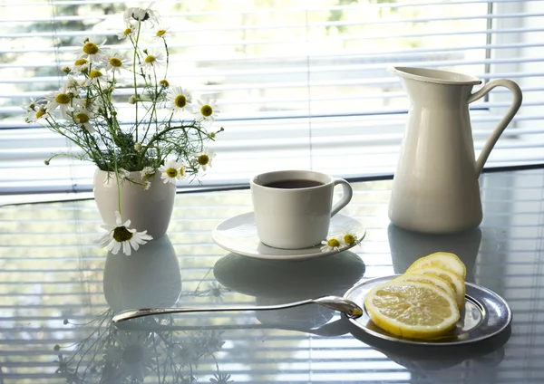 Daisies and cup of tea on glass table background window