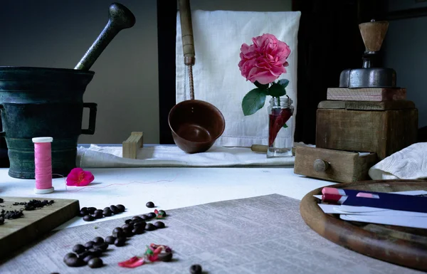 Still life. vintage.  items on the table: a cast-iron mortar, copper ladle mill for coffee or pepper, cutting board, pencils, paper, thread and  vase with pink vozoy,  beans  petals of rose
