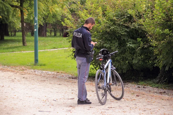 MILAN, ITALY - SEPTEMBER 29, 2015: A police officer with a bicycle standing in a park and looking at mobile phone