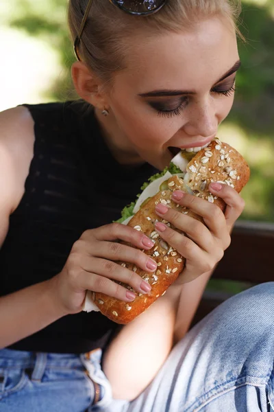 Hipster girt posing eating big sandwich
