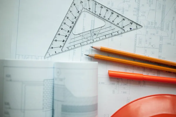 Architectural drawings of the house, ruler, pencils and construction orange helmet on a table