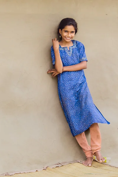 DIAMOND HARBOR, INDIA - APRIL 01, 2013 :Rural Indian girl with a beautiful smile in the blue dress posing near the wall