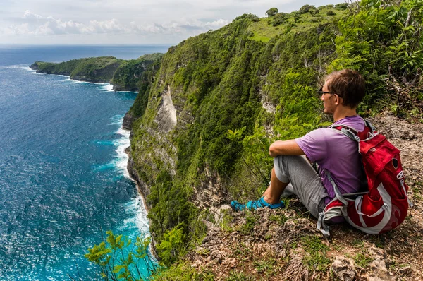 Hiker with backpack sitting on the top of the mountain and enjoy view