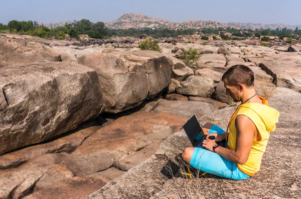 Young man sitting on the mountain with beautiful view and working with laptop