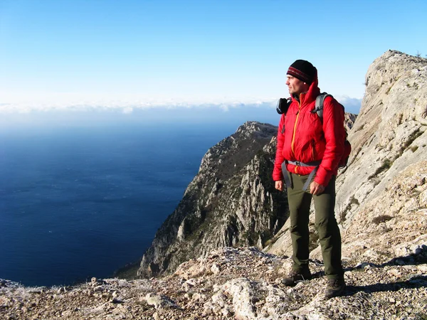 A man stands on a cliff looking at sea against the backdrop of mountains and sea.