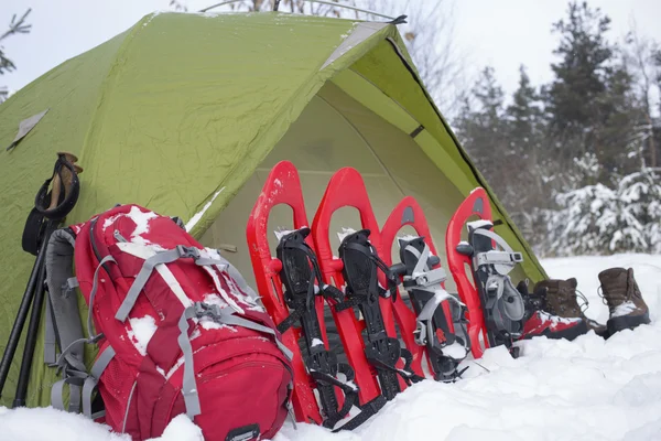Camping in a tent in the woods with a backpack and snowshoes.