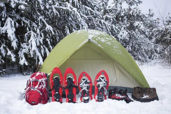Camping in a tent in the woods with a backpack and snowshoes.