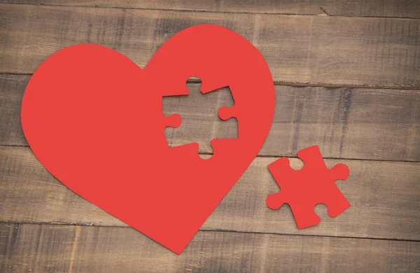 Incomplete puzzle in the shape of a heart on the wooden background