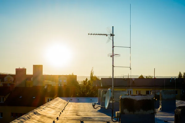 Simple antenna mast with antennas and satellite dish to receive digital TV signals, DVB-T, DVB-T2, DVB-S, DVB-S2 and FM radio signals and delayed lightning rod. Warm lighting.