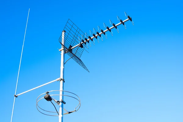 Simple antenna mast with antennas to receive digital TV and radio signals, DVB-T, DVB-T2 and FM (horizontal polarization) including delayed lightning rod. The background is pure blue sky.