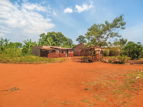 Brick house and other building with plain ground field before against plants and cloudy sky background. Jinja, Uganda.