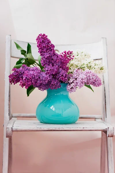 Still life with lilac flowers in vase turquoise placed on a wooden background