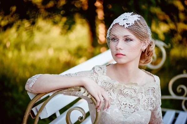 Beautiful blonde with a hairstyle and veil sitting on  bench, romantic looks