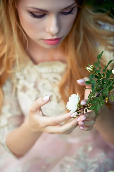 Girl in a light dress holding  rose on  branch. Tenderness
