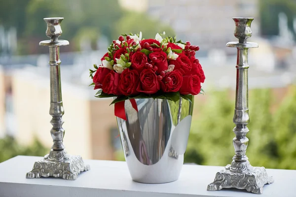 Dense red bouquet of roses and berries, brilliant in the iron bucket  two metal candle holders