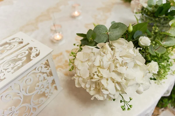 Wedding table decoration with white hydrangeas, a lace tablecloth and greens