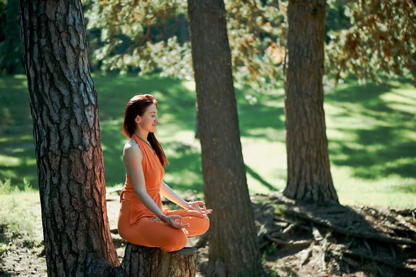 Young beautiful red-haired girl does yoga in Park on green background. .