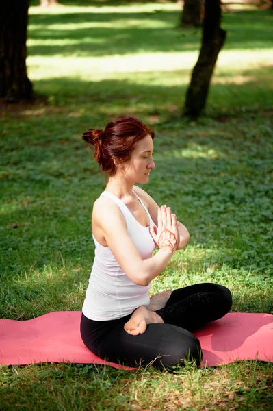 Young beautiful red-haired girl does yoga in Park on green background. .