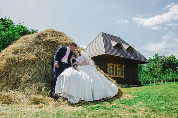 Couple in wedding attire with a bouquet of flowers and greenery is in the hands against the backdrop of the garden at sunset, the bride and groom