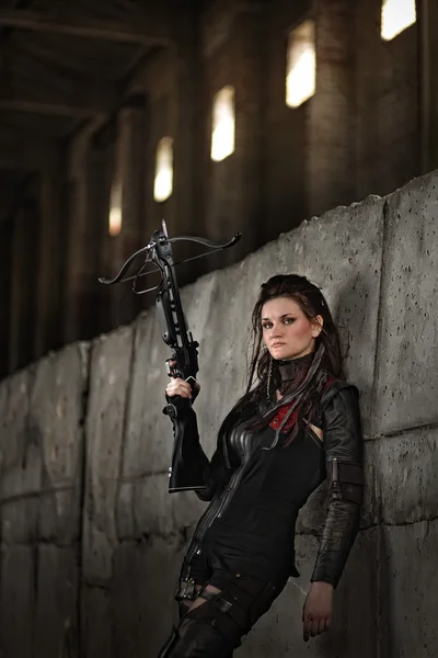 Raider girl in leather costume with a crossbow at post-apocalyptic world.