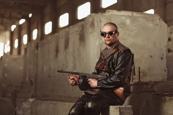 Portrait of a man from post-apocalyptic world with machine gun and the black glasses in an abandoned building