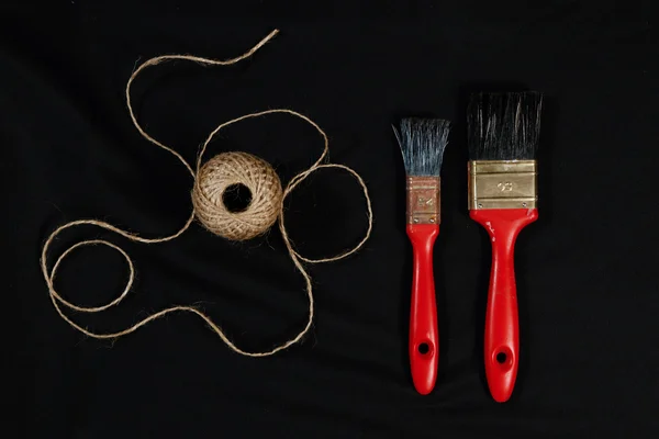 Packthread and two red  paint  brushes on black background