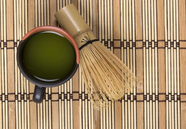 Green tea in clay cup with bamboo whisk