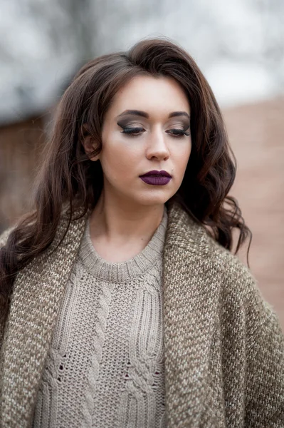 Spring in the country style. Full length portrait of young woman in white knitted sweater and furry hat standing in the front of rustic wood wall in the yard near house, wearing sweater casual.