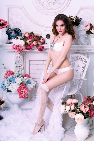 Beautiful young sexy woman , wearing white lingerie, room decorated with flowers. Perfect makeup. Beauty fashion. Eyelashes. Studio retouched shot.